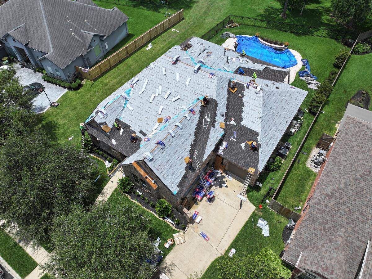Drone view of the crew laying underlayment and starting the new shingles, with the pool tarped off