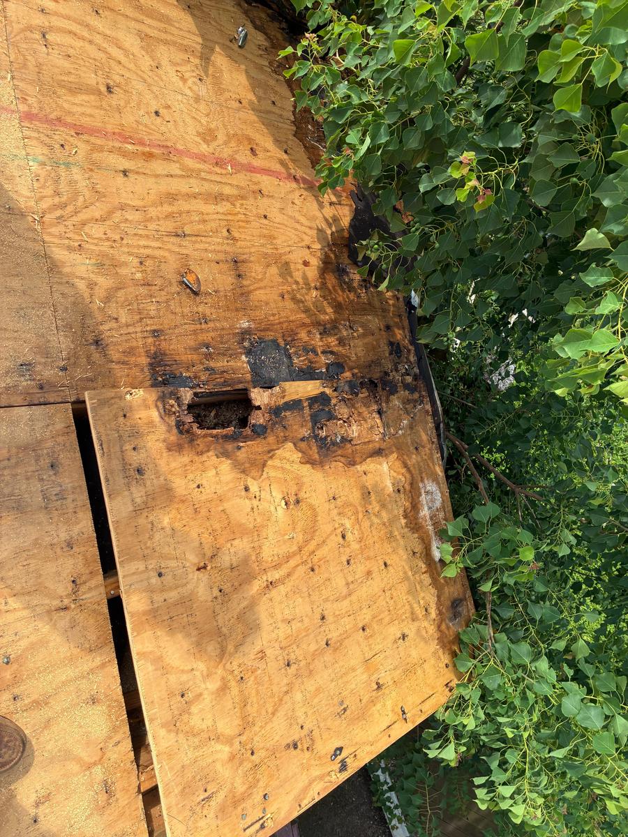 Rotted, water-stained roof decking with a hole worn through, exposed after tear-off