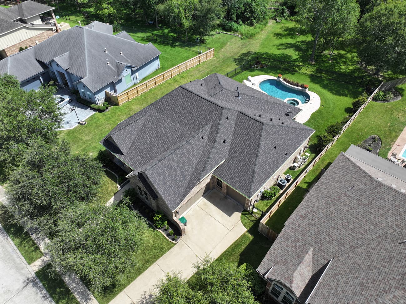 Drone view of a finished charcoal shingle roof by Salinas and Sons on a brick home with a backyard pool